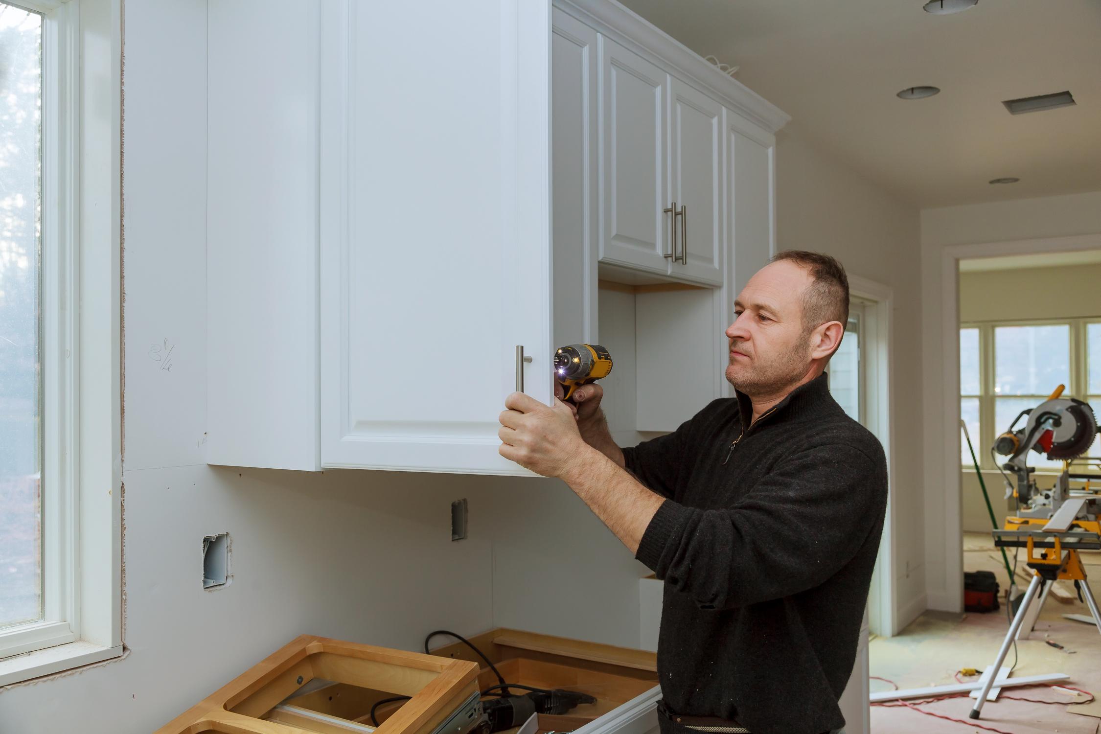 worker-sets-new-handle-white-cabinet-with-screwdriver-installing-kitchen-cabinets